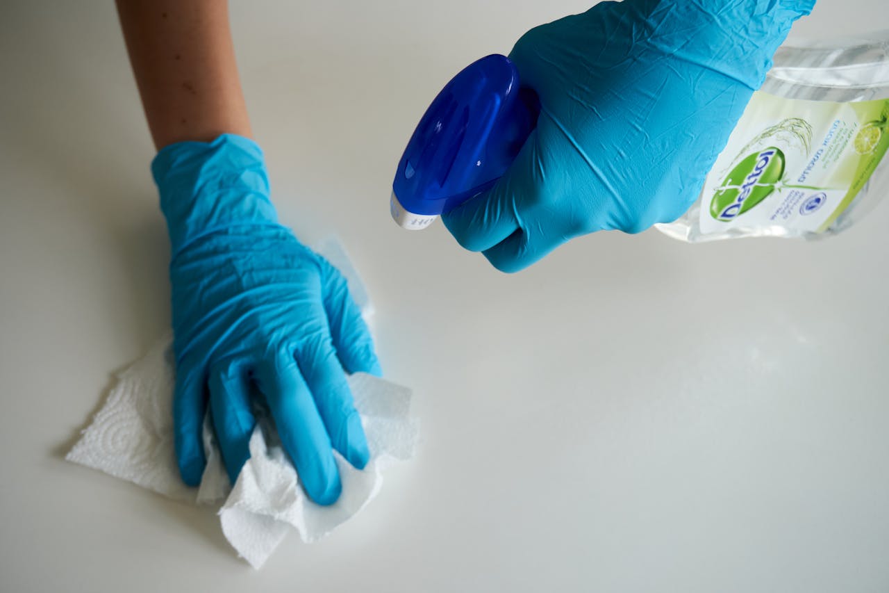 hero-img-01 Close-up of hands wearing gloves cleaning a surface with disinfectant spray.